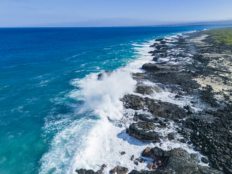 Aerial view of Kalaemamo coastline with turquoise waves crashing against black lava rocks and white sea foam under a clear blue sky Hawaii County Hawaii United States. Aerial view of Kalaemamo coastline with turquoise waves crashing against black lava rocks and white sea foam under a clear blue sky Hawaii County Hawaii United States.
