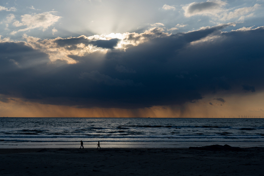 View of Strand Wijk aan Zee with silhouettes of people walking along the shore under dramatic sun rays breaking through dark clouds Wijk aan Zee North Holland Netherlands. View of Strand Wijk aan Zee with silhouettes of people walking along the shore under dramatic sun rays breaking through dark clouds Wijk aan Zee North Holland Netherlands.