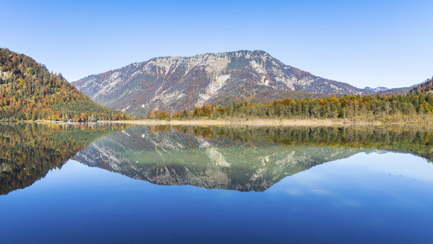 View of Offensee lake reflecting the surrounding mountains and vibrant autumn foliage under a clear blue sky in Ebensee Upper Austria Austria. View of Offensee lake reflecting the surrounding mountains and vibrant autumn foliage under a clear blue sky in Ebensee Upper Austria Austria.