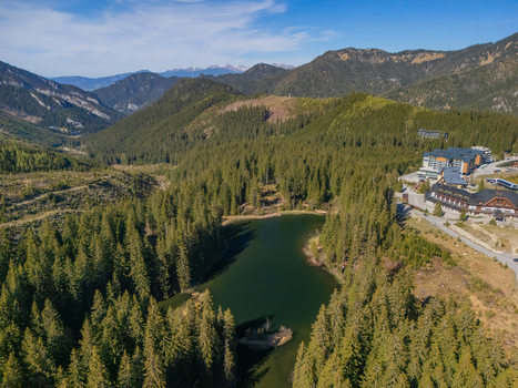 Aerial view of Vrbicke pleso lake surrounded by dense pine forests and the Low Tatra mountains under a clear sky Demanovska Dolina Zilina Region Slovakia. Aerial view of Vrbicke pleso lake surrounded by dense pine forests and the Low Tatra mountains under a clear sky Demanovska Dolina Zilina Region Slovakia.