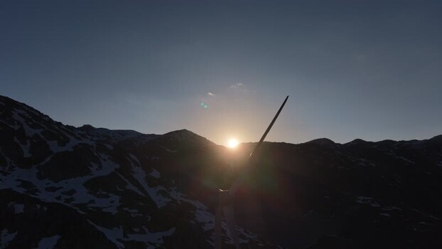 Aerial view of San Gottardo wind Park with wind turbine blades silhouetted against the sun over snowy mountain peaks in Airolo Ticino Switzerland.