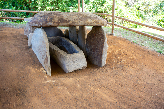 View of an ancient stone sarcophagus at San Agustin Archaeological Park with weathered rock slabs and a protective bamboo fence in San Agustin Huila Colombia.