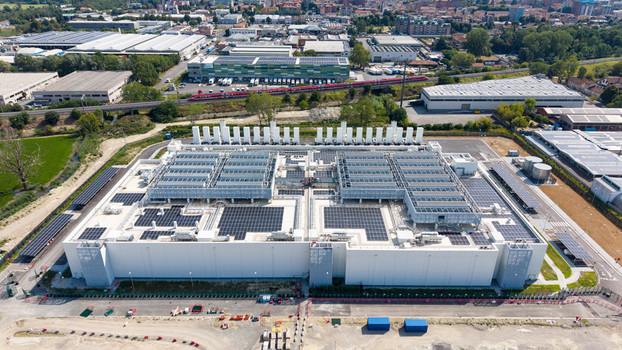 Aerial view of a modern hyperscale data center with extensive rooftop solar panels and cooling infrastructure located in an industrial area near a railway line in Melegnano Lombardy Italy.
