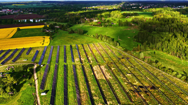 Aerial view of solar farm with rows of photovoltaic panels set in a lush green rural landscape with a vibrant yellow rapeseed field and surrounding forest in Latvia. Aerial view of solar farm with rows of photovoltaic panels set in a lush green rural landscape with a vibrant yellow rapeseed field and surrounding forest in Latvia.