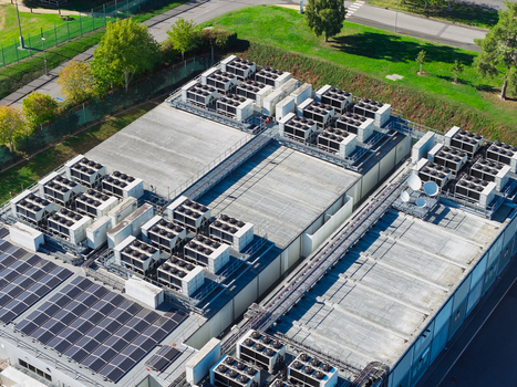 Aerial view of a data center roof featuring numerous HVAC cooling units rows of solar panels and satellite dishes set within a fenced industrial perimeter in the United Kingdom.