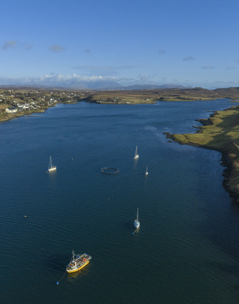 Aerial view of Loch Dunvegan with sailboats and a yellow fishing boat anchored in the blue water surrounded by rolling hills Dunvegan Scotland United Kingdom. Aerial view of Loch Dunvegan with sailboats and a yellow fishing boat anchored in the blue water surrounded by rolling hills Dunvegan Scotland United Kingdom.