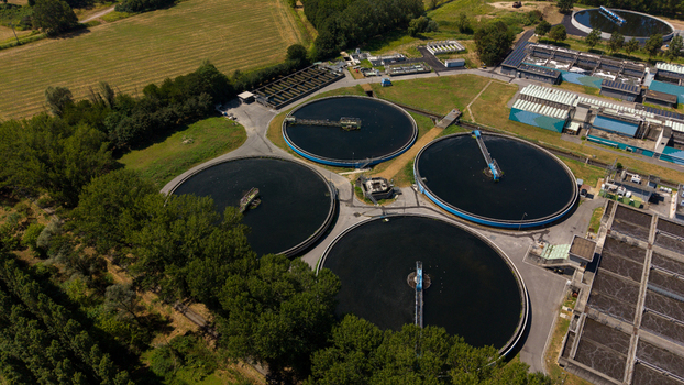 Aerial view of a wastewater treatment plant featuring large circular sedimentation tanks and industrial infrastructure surrounded by green trees and fields in Milan Lombardy Italy. Aerial view of a wastewater treatment plant featuring large circular sedimentation tanks and industrial infrastructure surrounded by green trees and fields in Milan Lombardy Italy.
