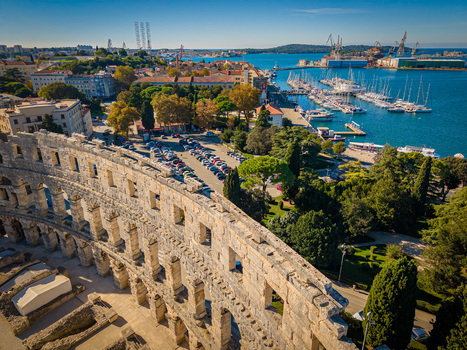 Aerial view of the ancient Roman amphitheater standing proudly against the azure Adriatic Sea with boats gently bobbing in the harbor Pula Istria County Croatia.