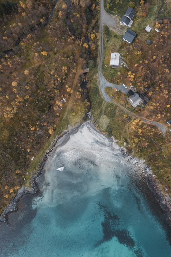 Aerial view of the coastal landscape of Senja with a sandy beach turquoise waters rocky shoreline and autumn colored vegetation surrounding houses in Senja Troms Norway.