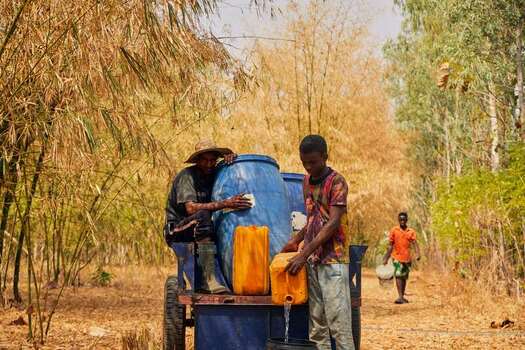 Kundu Federal Capital Terri Nigeria 19 September 2026 View of workers at SCL Agroindustrial Farm filling water containers from a cart amidst dry vegetation. Kundu Federal Capital Terri Nigeria 19 September 2026 View of workers at SCL Agroindustrial Farm filling water containers from a cart amidst dry vegetation.