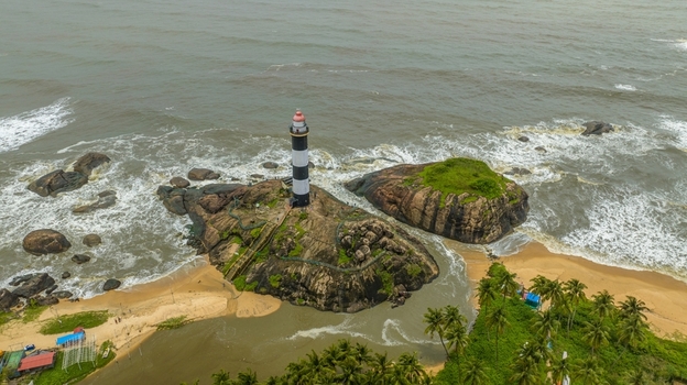 Aerial view of Kapu Light House standing on a rocky outcrop surrounded by the Arabian Sea sandy beach and lush palm trees in Udupi Karnataka India.