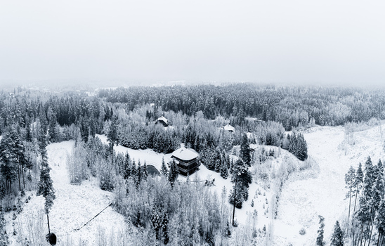 Aerial view of a secluded house nestled within a dense forest covered in fresh snow under a cloudy winter sky Latvia. Aerial view of a secluded house nestled within a dense forest covered in fresh snow under a cloudy winter sky Latvia.