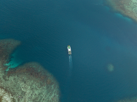 Aerial view of a lone ferry cuts through the deep blue sea contrasting vividly with the lighter turquoise shallows and coral reefs Karimunjawa Jawa Tengah Indonesia. Aerial view of a lone ferry cuts through the deep blue sea contrasting vividly with the lighter turquoise shallows and coral reefs Karimunjawa Jawa Tengah Indonesia.