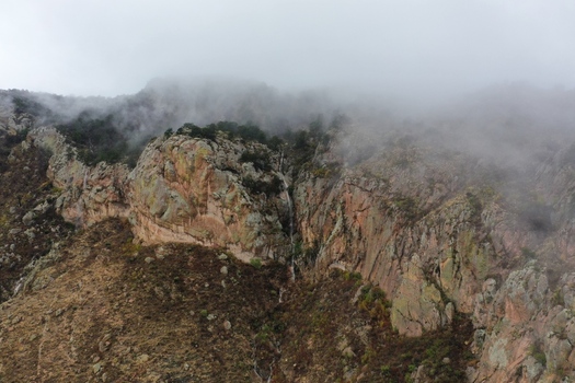 Aerial view of the rocky cliffs and waterfall of Sierra de San Miguelito Norte shrouded in mist and low clouds in San Luis Potosi San Luis Potosi Mexico. Aerial view of the rocky cliffs and waterfall of Sierra de San Miguelito Norte shrouded in mist and low clouds in San Luis Potosi San Luis Potosi Mexico.