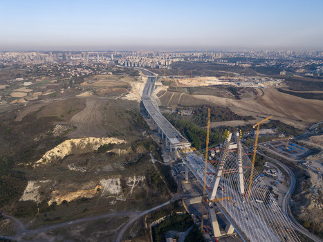 Aerial view of a large cable stayed bridge under construction with tall pylons and cranes spanning over a rural landscape with a distant city skyline in Istanbul Istanbul Turkiye.