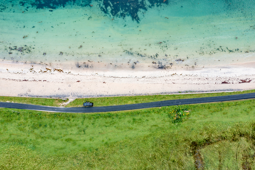 Aerial view of St John s Point Beach with a car parked on the coastal road turquoise water and green fields in Dunkineely County Donegal Ireland.