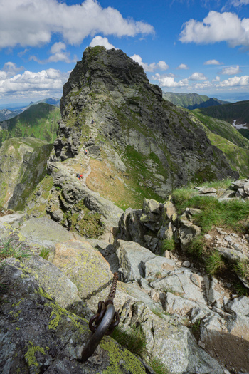 View of Tri kopy in Western Tatras featuring a rocky mountain ridge with hiking trail safety chains and hikers under a blue sky in Ziar Zilina Region Slovakia. View of Tri kopy in Western Tatras featuring a rocky mountain ridge with hiking trail safety chains and hikers under a blue sky in Ziar Zilina Region Slovakia.
