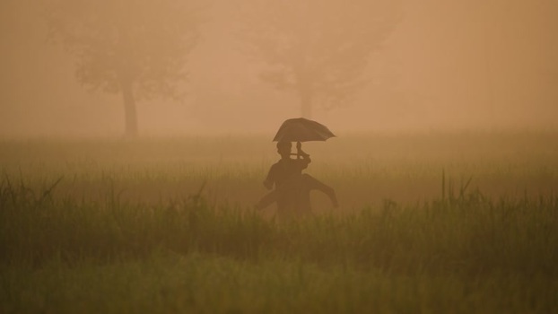 View of people with an umbrella in a misty field Bangladesh.