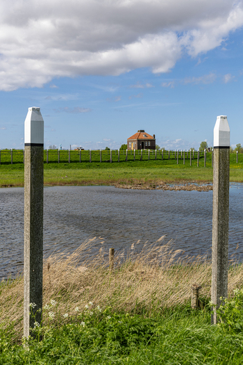 View of the historic former island of Schokland with wooden poles a calm pond and a traditional brick house on a grassy embankment Schokland Flevoland Netherlands.