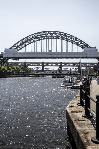 View of the iconic Tyne Bridge spanning the River Tyne with other historic bridges in the background seen from the paved waterfront in Newcastle upon Tyne England United Kingdom. View of the iconic Tyne Bridge spanning the River Tyne with other historic bridges in the background seen from the paved waterfront in Newcastle upon Tyne England United Kingdom.