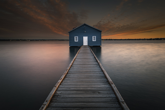 View of the iconic Blue Boat House at the end of a long wooden jetty over the calm waters of the Swan River at sunset in Crawley Western Australia Australia. View of the iconic Blue Boat House at the end of a long wooden jetty over the calm waters of the Swan River at sunset in Crawley Western Australia Australia.
