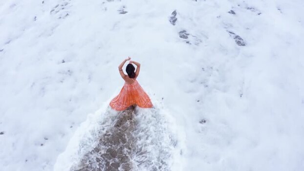 Aerial view of a woman in an orange dress standing in sea foam Indonesia. Aerial view of a woman in an orange dress standing in sea foam Indonesia.