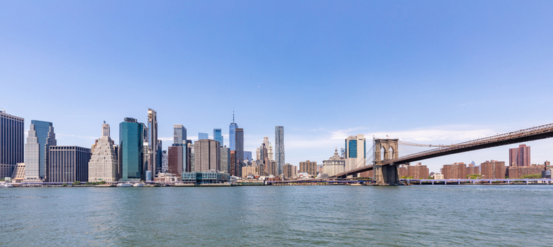 View of the Brooklyn Bridge and the Manhattan skyline across the East River under a clear blue sky in New York New York United States. View of the Brooklyn Bridge and the Manhattan skyline across the East River under a clear blue sky in New York New York United States.
