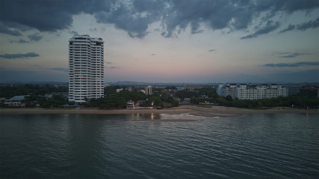 Aerial view of Jomtien Beach featuring a tall white skyscraper and coastal buildings under a twilight sky in Chon Buri Thailand.