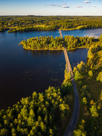 Aerial view of a road crossing a lake via a bridge surrounded by dense forest in the golden hour light in Gallared Halland County Sweden. Aerial view of a road crossing a lake via a bridge surrounded by dense forest in the golden hour light in Gallared Halland County Sweden.
