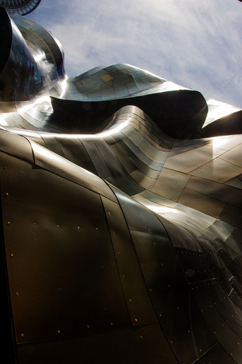 View of the metallic undulating exterior of the Museum of Pop Culture featuring curved panels and rivets under a bright sky in Seattle Washington United States.