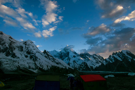 View of Masherbrum peak with snow covered slopes and base camp tents under a cloudy blue sky in Skardu Gilgit Pakistan. View of Masherbrum peak with snow covered slopes and base camp tents under a cloudy blue sky in Skardu Gilgit Pakistan.