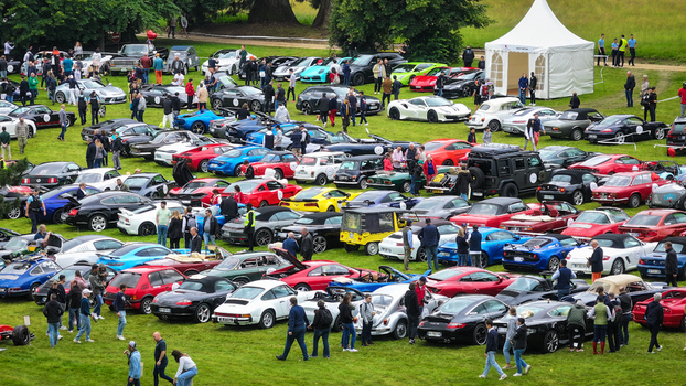 La Chapelle de Guinchay France 01 June 2024 Aerial view of a large collection of luxury sports cars and classic vehicles parked on a green field with people walking around.