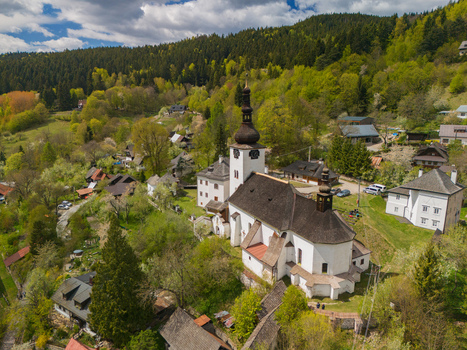 Aerial view of the historic Church of the Conversion of the Lord and traditional houses surrounded by lush green forests and rolling hills in Spania Dolina Banska Bystrica Region Slovakia.