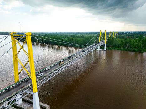 Aerial view of Barito Bridge with yellow suspension towers spanning the Barito River featuring traffic on the deck and lush green riverbanks in Kecamatan Alalak Kalimantan Selatan Indonesia. Aerial view of Barito Bridge with yellow suspension towers spanning the Barito River featuring traffic on the deck and lush green riverbanks in Kecamatan Alalak Kalimantan Selatan Indonesia.
