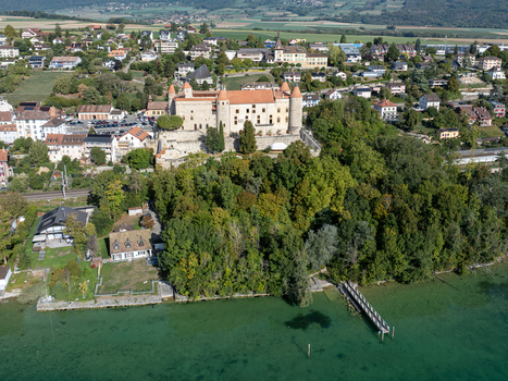 Aerial view of the historic Chateau de Grandson overlooking the lake with surrounding trees residential buildings and a small pier in Grandson Vaud Switzerland.