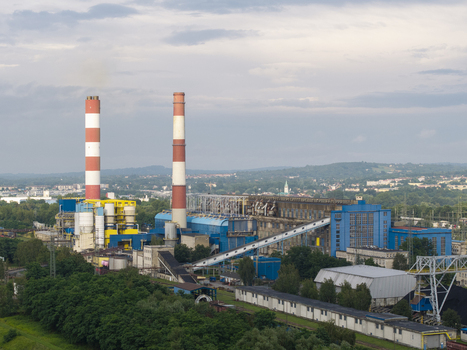 Aerial view of the industrial power plant with two tall red and white chimneys conveyor belts and blue buildings surrounded by green trees in Krakow Lesser Poland Voivode Poland.