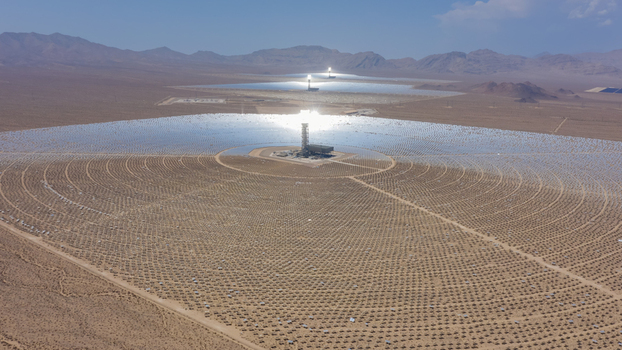 Aerial view of a large concentrated solar power plant with thousands of mirrors and a central solar tower in a vast desert landscape under a clear blue sky United States.