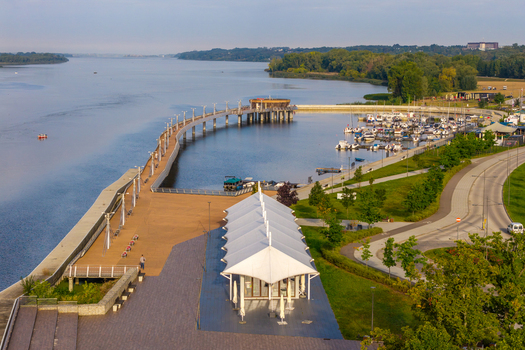 Aerial view of the Vistula river featuring a modern pier a marina with moored boats a promenade and a white tent structure along the waterfront in Plock Masovian Voivodeship Poland. Aerial view of the Vistula river featuring a modern pier a marina with moored boats a promenade and a white tent structure along the waterfront in Plock Masovian Voivodeship Poland.