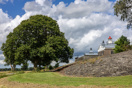 View of Lichtwachterswoning Oud Kraggenburg on a stone embankment with a large tree under a cloudy sky Kraggenburg Flevoland Netherlands. View of Lichtwachterswoning Oud Kraggenburg on a stone embankment with a large tree under a cloudy sky Kraggenburg Flevoland Netherlands.