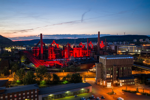 Volklingen Germany 09 May 2026 Aerial view of the Volklingen Ironworks illuminated with red lights at twilight with industrial chimneys and surrounding urban landscape. Volklingen Germany 09 May 2026 Aerial view of the Volklingen Ironworks illuminated with red lights at twilight with industrial chimneys and surrounding urban landscape.