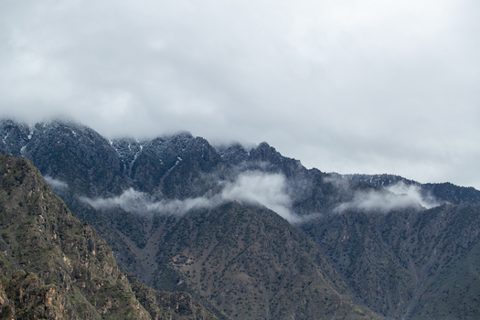 View of snow capped mountain peaks partially covered by thick white clouds and mist over rocky slopes Chilas Gilgit Pakistan. View of snow capped mountain peaks partially covered by thick white clouds and mist over rocky slopes Chilas Gilgit Pakistan.