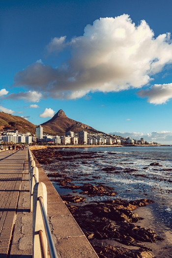 View of Lion s Head mountain rising above the city skyline and Sea Point promenade with people walking along the rocky coast in Cape Town Western Cape South Africa. View of Lion s Head mountain rising above the city skyline and Sea Point promenade with people walking along the rocky coast in Cape Town Western Cape South Africa.