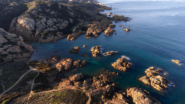 Aerial view of Cala Sarraina featuring rugged rock formations turquoise waters and coastal trails during golden hour in Trinita d Agultu e Vignola Sardinia Italy. Aerial view of Cala Sarraina featuring rugged rock formations turquoise waters and coastal trails during golden hour in Trinita d Agultu e Vignola Sardinia Italy.