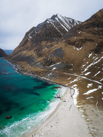 Aerial view of turquoise waters meeting the sandy shore beneath the rugged snow dusted peaks of Uttakleivveien creating a dramatic contrast Haukland Beach Nordland Norway. Aerial view of turquoise waters meeting the sandy shore beneath the rugged snow dusted peaks of Uttakleivveien creating a dramatic contrast Haukland Beach Nordland Norway.