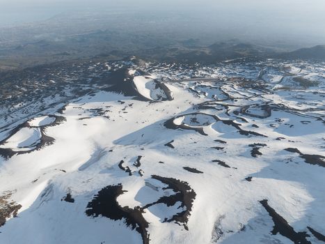 Aerial view of snow covered volcanic craters and dark lava flows on the southern slope of Mount Etna in Nicolosi Sicilia Italy. Aerial view of snow covered volcanic craters and dark lava flows on the southern slope of Mount Etna in Nicolosi Sicilia Italy.