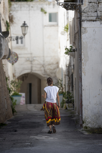 View of a woman walking through a narrow alleyway with white washed buildings and traditional street lamps in the historic old town of Ostuni Apulia Italy. View of a woman walking through a narrow alleyway with white washed buildings and traditional street lamps in the historic old town of Ostuni Apulia Italy.