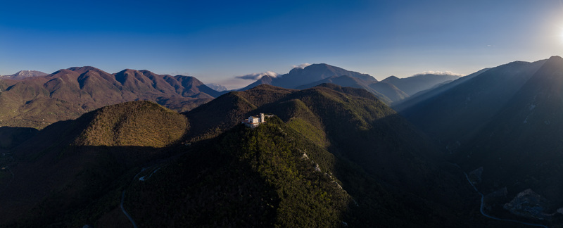 Aerial view of Santuario del Santissimo Salvatore perched on a mountain peak surrounded by the lush green Picentini mountains under a clear blue sky Montella Campania Italy. Aerial view of Santuario del Santissimo Salvatore perched on a mountain peak surrounded by the lush green Picentini mountains under a clear blue sky Montella Campania Italy.