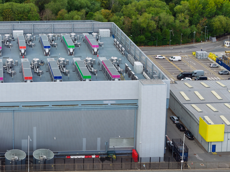 Aerial view of a data center featuring rooftop cooling units with colorful accents adjacent parking lot and industrial facility in the United Kingdom.