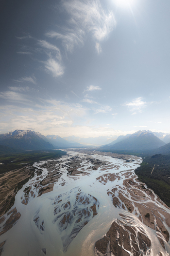 Aerial view of the braided river system flowing through the Alaska Wilderness surrounded by snow capped mountains under a bright sky in Palmer Alaska United States. Aerial view of the braided river system flowing through the Alaska Wilderness surrounded by snow capped mountains under a bright sky in Palmer Alaska United States.