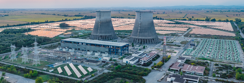Aerial view of an industrial power complex featuring two large cooling towers extensive solar panel arrays and battery storage units set within a rural landscape in Italy. Aerial view of an industrial power complex featuring two large cooling towers extensive solar panel arrays and battery storage units set within a rural landscape in Italy.